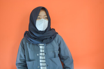 A Muslim Asian woman wearing a jacket and hijab. Looking to the left. Orange background