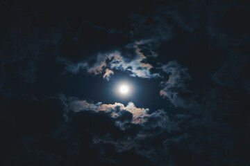 The moon shines through the clouds in the night sky.