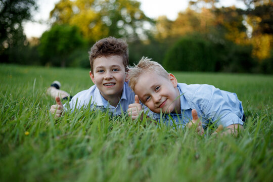 Front image of a funny kids lie on grass in the park, looking at camera.