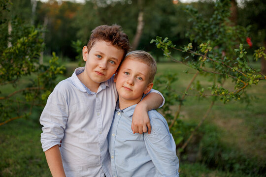 Two cute brothers hugging, dressed in shirts, posing in the park.