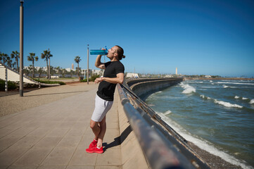 Young athletic man, sportsman, resting, drinking water after a workout outdoor.