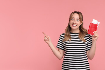 Happy young woman with passport and ticket pointing at something on pink background, space for text