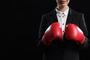 Businesswoman in suit wearing boxing gloves on black background, closeup. Space for text