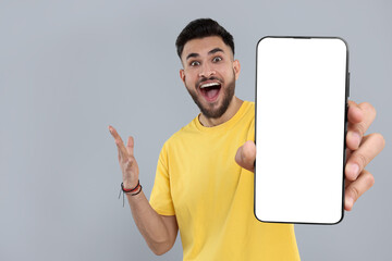 Happy man holding smartphone with empty screen on grey background, space for text