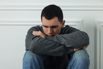 Sad man sitting near white wall indoors