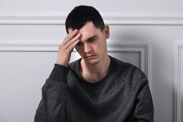 Sad man sitting near white wall indoors
