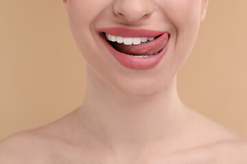 Young woman licking her teeth on beige background, closeup