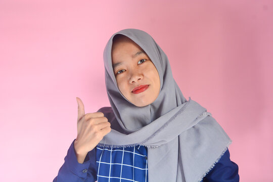 Copy space. A young Indonesian woman in blue clothes and gray hijab posing in front, looking to the left and pointing something in the same direction and full of confidence