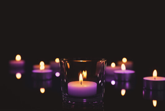 Beautiful burning violet wax candles on black background. Funeral attributes