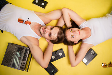 A man and a woman lie on a yellow background and listen to retro music. An old tape recorder and...