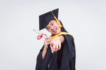 Cheerful young woman in graduation cap and gown, pointing at the camera, celebrating her science...