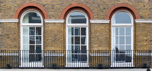  balcony with classic white arch windows of typical london architecture with red brick wall	