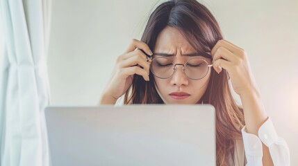 Young Asian woman are stressed and tired from work. She was holding glasses at a white desk with a laptop in the office.