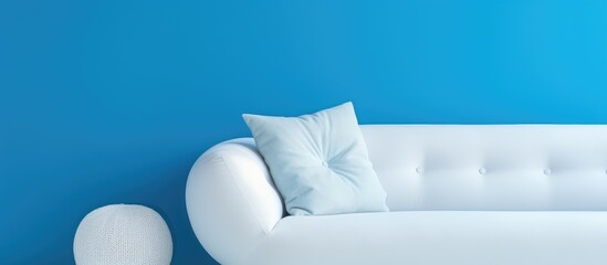 A white couch with a round pillow is placed against a blue wall. The contrast between the white sofa and the blue wall creates a visually appealing setting.