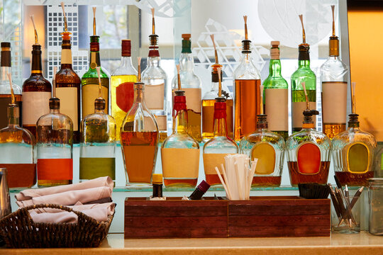 Liquor bottles in many different colors and shapes sitting on a bar without labels