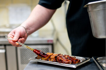 Professional chef in a commercial kitchen applying sauce to grilled ribs. The image showcases the preparation of delicious barbecue