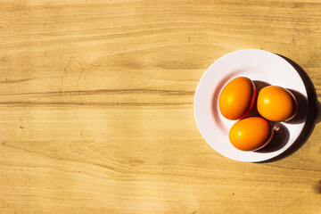 White plate with 3 chicken eggs on wooden background