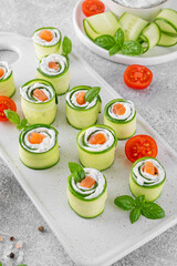 Cucumbers rolls with cream cheese, salted salmon and fresh herbs served on a white ceramic board on a concrete background. Selective focus