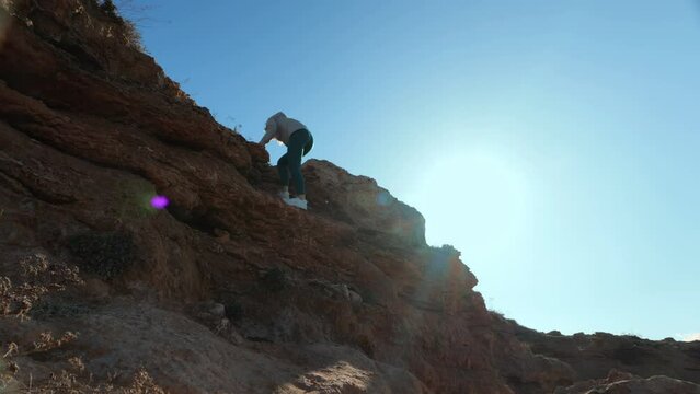 The determined girl, clad in sportswear, courageously climbs the mountain, her every step a testament to her strength and perseverance amidst the vast expanse of the azure sky