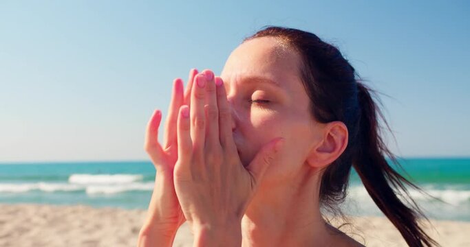 Woman applying spf sun cream uv protection on her face to protect from sun on the sunny beach. Close-up shot