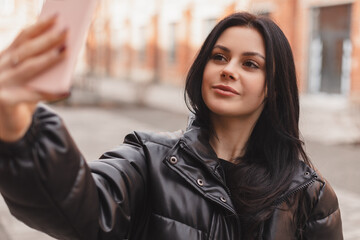 Pensive brunette woman make selfie posing on street brick building background. Outdoor shot of...