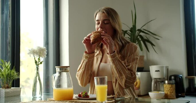 a woman is sitting at a table eating a sandwich and drinking orange juice