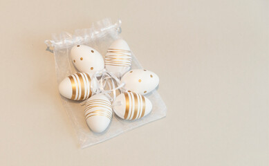 White Easter eggs decorated with gold color on a storage bag on a gray background.