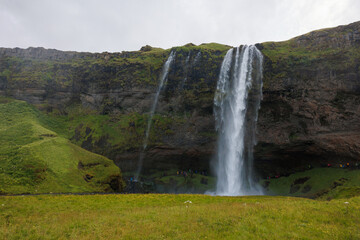 Seljalandsfoss, a famous and unique waterfall in Iceland with visitors walking behind the falls into a small cave. Trip concept.