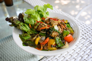 A traditional Thai dish, stir-fried black pepper barramundi, with colorful bell peppers and fresh vegetables on a white plate.
