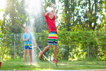 Kids play with water sprinkle hose. Summer garden