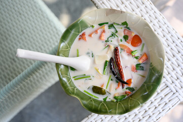 A bowl of Tom Kha, a traditional Thai coconut soup with mixed seafood, served in a green ceramic...