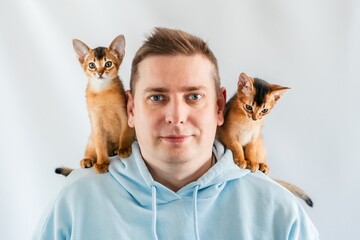 Smiling funny man in blue hoodie with twin Abyssinian cats, small newborn kittens sitting on...