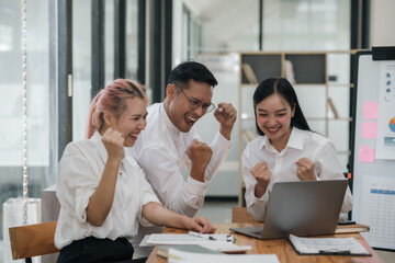 Three ecstatic asian business professionals celebrating a victory with a fist pump in a modern...