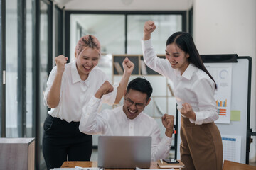 Three ecstatic asian business professionals celebrating a victory with a fist pump in a modern...