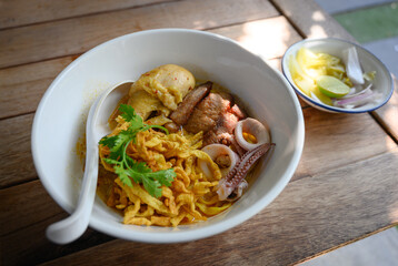 A bowl of Khao Soi, a Northern Thai coconut curry noodle soup with chicken, seafood, and crispy noodles, served with lime and pickled vegetables.
