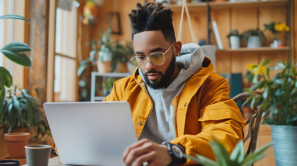 Obraz premium Handsome young African American man sitting on the chair in the room at a house or home, and using a laptop or notebook. Male adult freelancing, working online on the internet