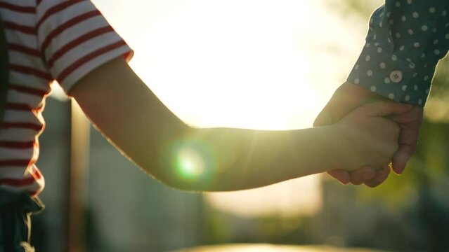 Happy family mother and daughter holding hands walking together at bright sun light summer park closeup. Little baby kid child and female parent arm enjoy outdoor weekend activity with love tenderness