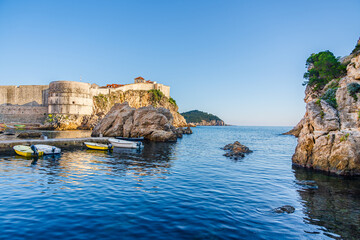 Dubrovnik medieval walls at the West Harbour beach on the shores of the Adriatic Sea; Mediteranean Sea riviera in Dubrovnik, Croatia - 754975024