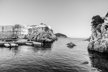 Dubrovnik medieval walls at the West Harbour beach on the shores of the Adriatic Sea; Mediteranean Sea riviera in Dubrovnik, Croatia in black and white - 754975282
