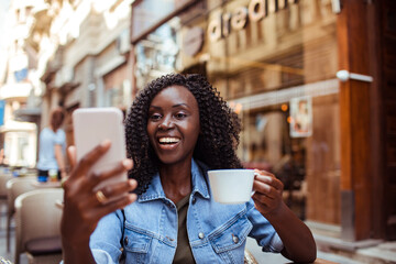 African American woman taking a selfie with coffee at a street cafe