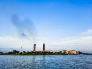 High pollution from power plant. Power plant on the coast. Ecology disaster concept. Power plant high pipes with black smoke moving up polluting atmosphere.