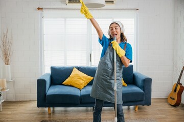 Happy Asian housewife finds joy in cleaning singing her favorite song using mop as microphone...