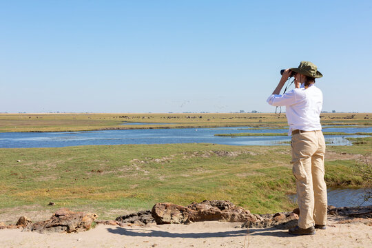 Tourist watching wildlife by binocular on Chobe River at sunrise. Chobe National Park, famous wildlilfe reserve and upscale travel destination in Namibia, Africa. Toned image.