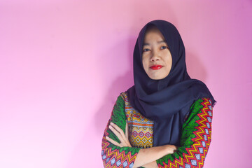 Portrait of beautiful Asian or Indonesian woman wearing green batik dress having creative idea, smiling face, surprised expression pointing finger up on copy space isolated on pink background