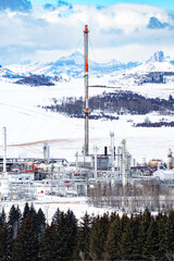 Winter Gas plant with flare stack overlooking the Canadian Rocky Mountains and snow covered agriculture fields West of Cochrane Alberta Canada.