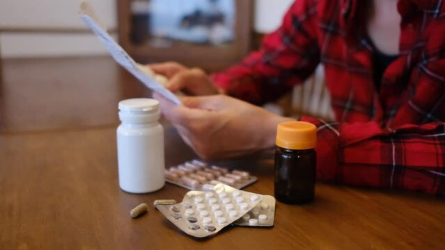 Close-up capturing woman's hands gripping medical prescription, wooden table displaying scattered pills and medicine bottles, emphasizing healthcare medication management
