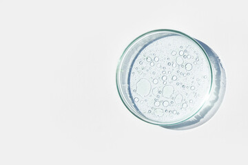 Petri dish. Petri's cup with liquid. Chemical elements, oil, cosmetics. Gel, water, molecules, viruses. Close-up. On a white background.