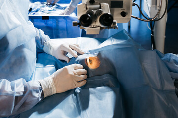 Vision correction with microscope. Surgeon's hands in gloves performing laser eye vision...