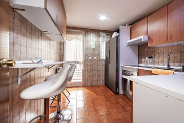 Apartment with kitchen with brown furniture, white countertop, stools with chrome legs, large...