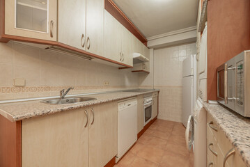 Fototapeta na wymiar Front image of kitchen with used light wood furniture, matching stoneware floors, tiled walls